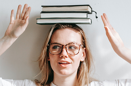 Person wearing glasses and balancing a stack of books on their head