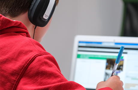 A student wearing a red sweatshirt and headphones and using a computer