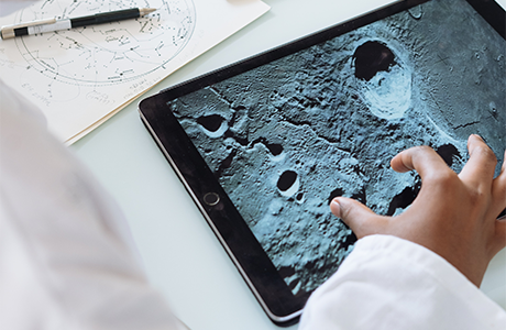 A person's hand on a tablet computer displaying an image of the moon