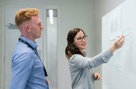 A person showing another person information on a white board