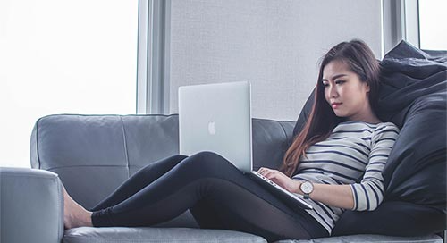 Woman lounged on a couch and working on her laptop