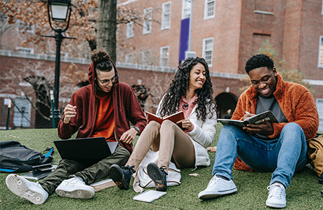 Three university students studying on campus lawn. 