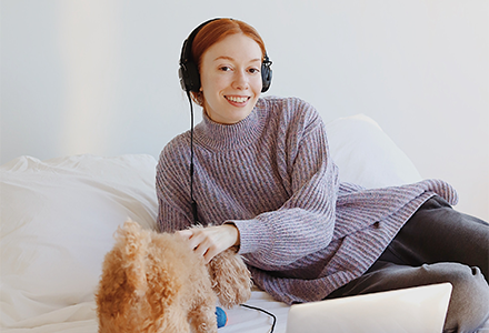 Woman working on her computer in bed and comforting her dog