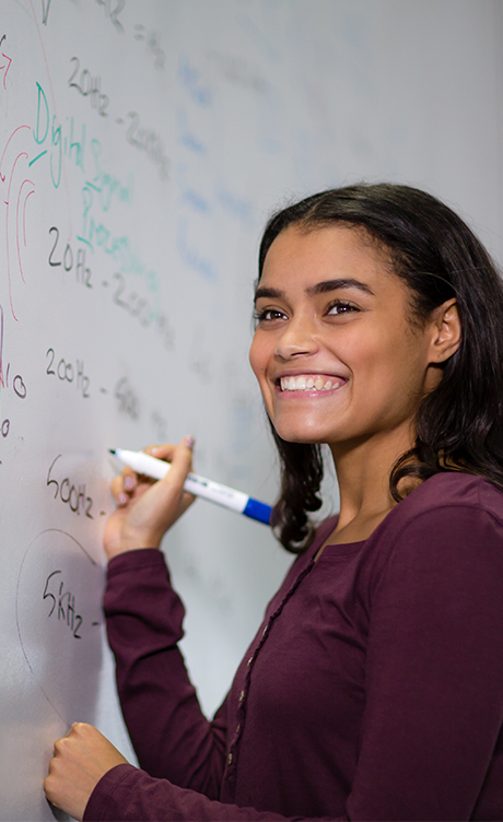 Student smiling while writting on a whiteboad